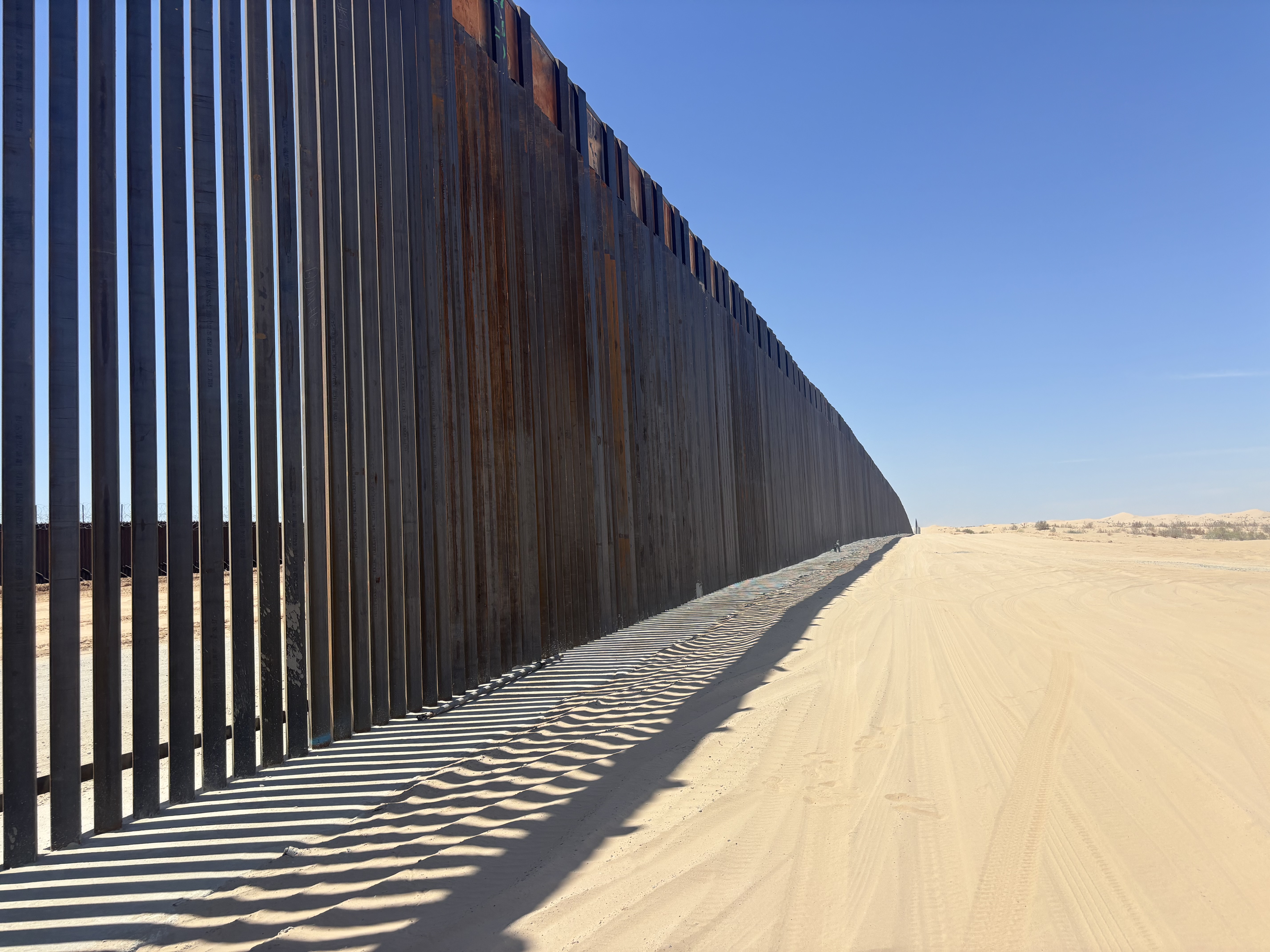 Long perspective view of the steel border fence stretching across the California desert