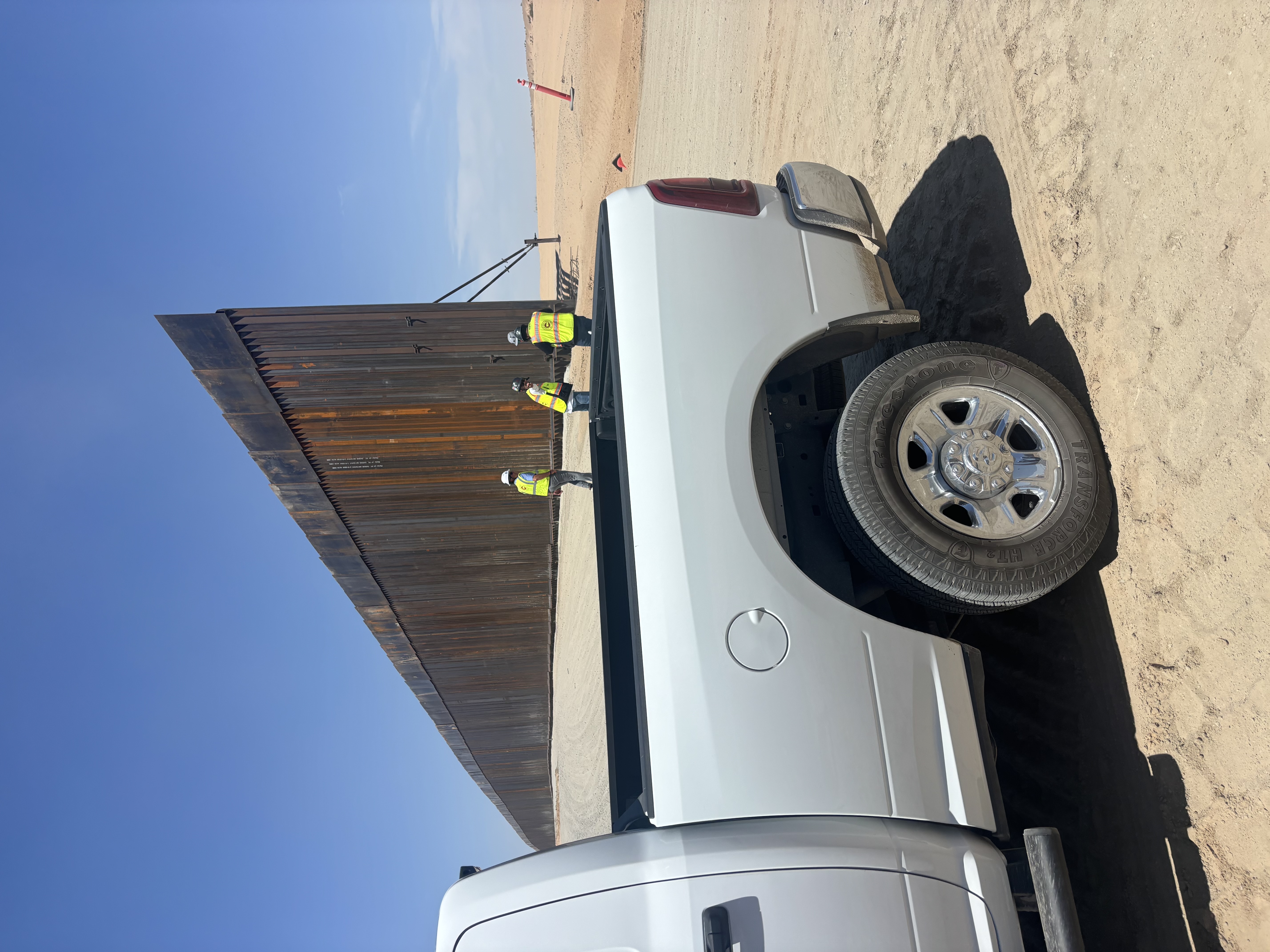 Wide view of the border fence, work vehicles, and site crew in the California desert